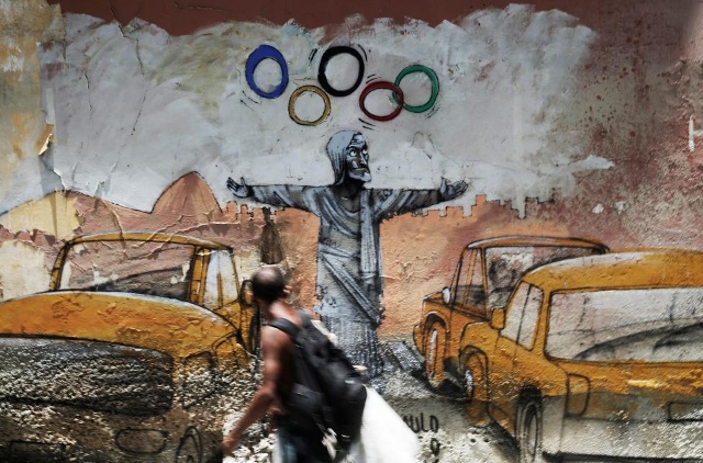 Một người đàn ông đi qua một graffiti của nghệ sĩ người Brazil Paulo Ito miêu tả các bức tượng của Chúa Kitô Đấng Cứu Chuộc tung hứng các vòng tròn Olympic tại Rio de Janeiro, Brazil, tháng 16, năm 2017