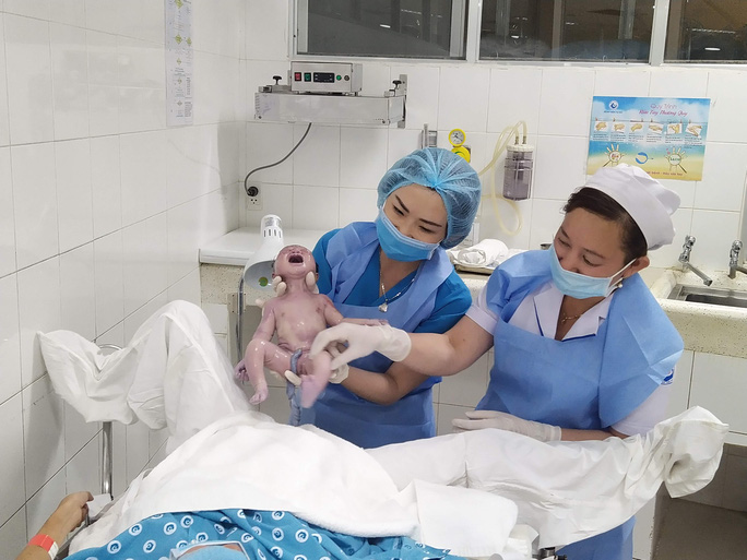 Bác sĩ và nữ hộ sinh giơ bé gái vừa chào đời lên khiến một sản phụ bật khóc