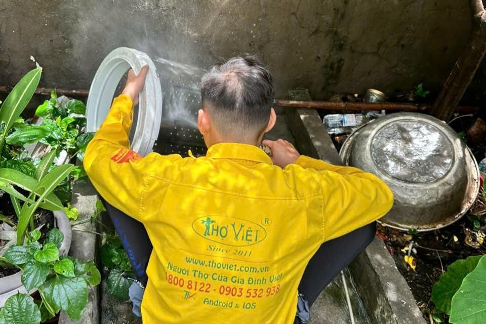 A person in a yellow jacket washing a metal objectDescription automatically generated