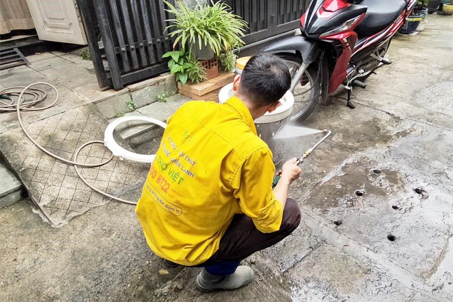 A person kneeling on the ground with a hose and a bucket of waterDescription automatically generated